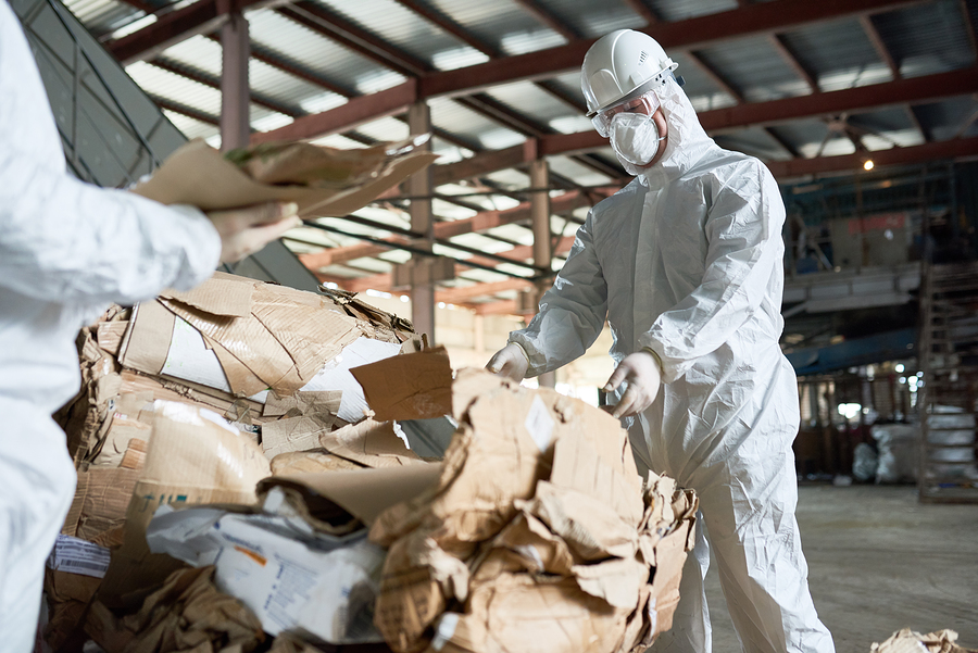 PureHaven Asbestos Removal - Services Portrait of factory worker wearing biohazard suit sorting recyclable cardboard on waste processing plant, copy space