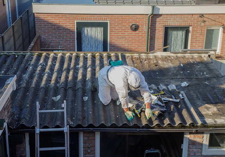 Professional asbestos removal. Men in protective suits are removing asbestos cement corrugated roofing